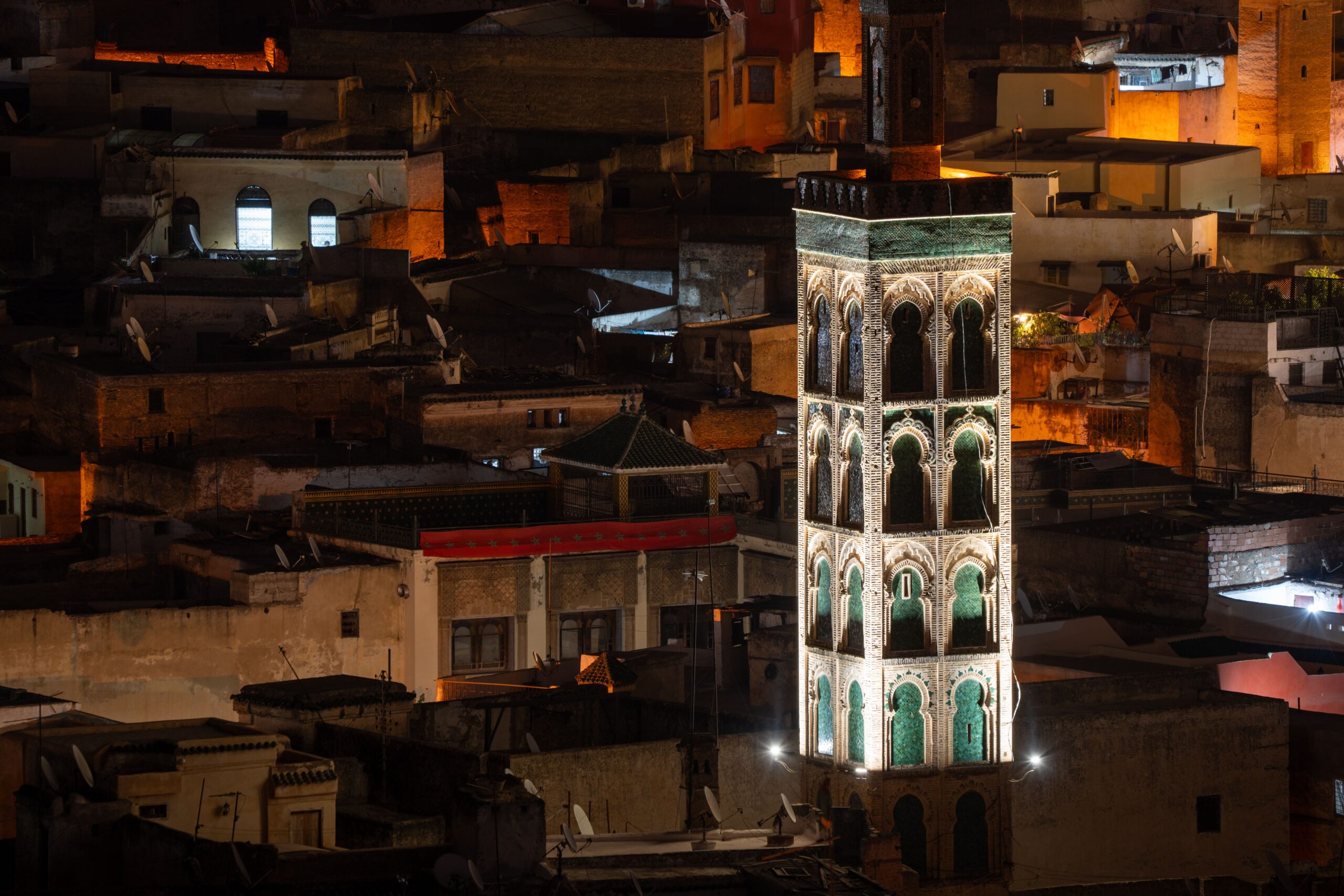 A beautifully lit tower stands out amidst the historic buildings of Fez at night.