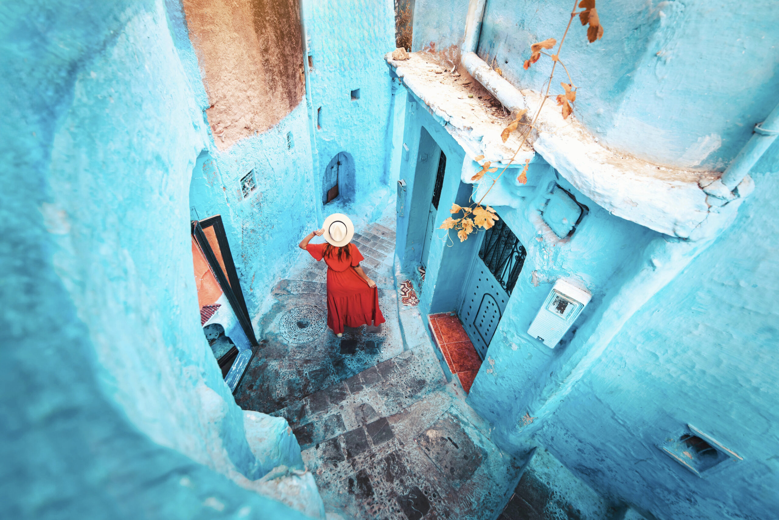 Young woman with red dress visiting the blue city Chefchaouen, Marocco - Happy tourist walking in Moroccan city street - Travel and vacation lifestyle concept